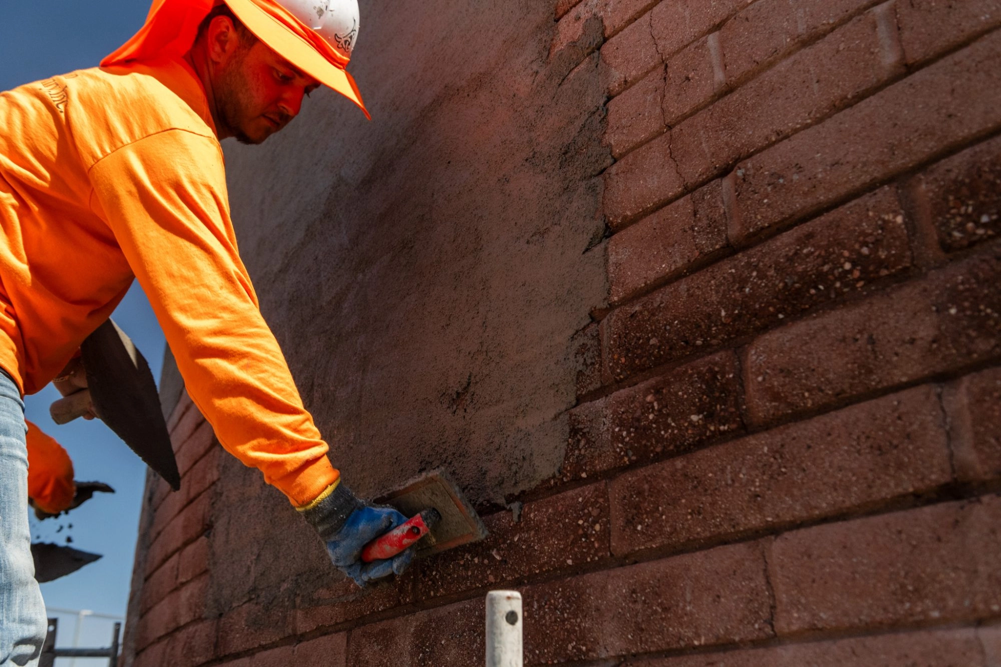 Father and Son Masonry worker hand troweling stucco onto curved brick wall at Grass Clippings Rolling Hills AZ