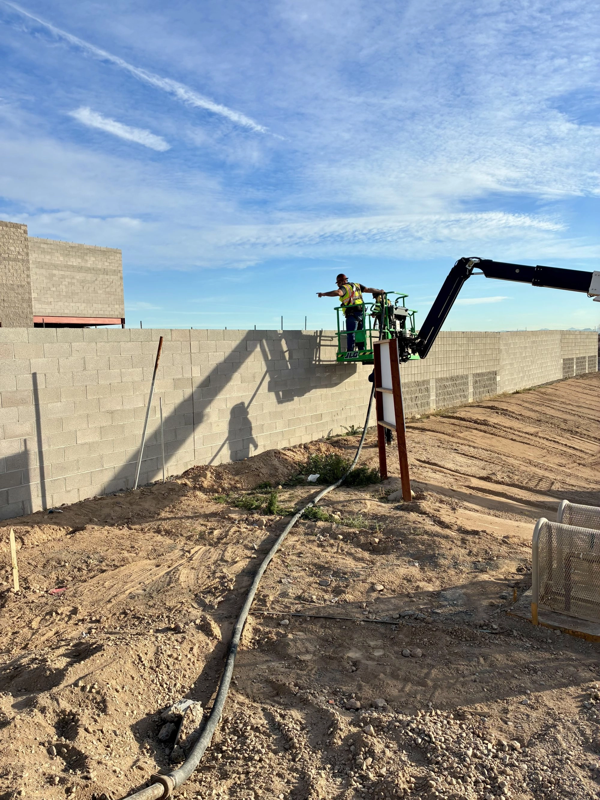 Worker on JLG aerial lift inspecting completed CMU perimeter wall at Sunbelt Rentals El Mirage AZ